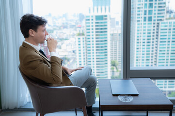 Young businessman sit and relax in the relaxation room by the window overlooking the beautiful city buildings.