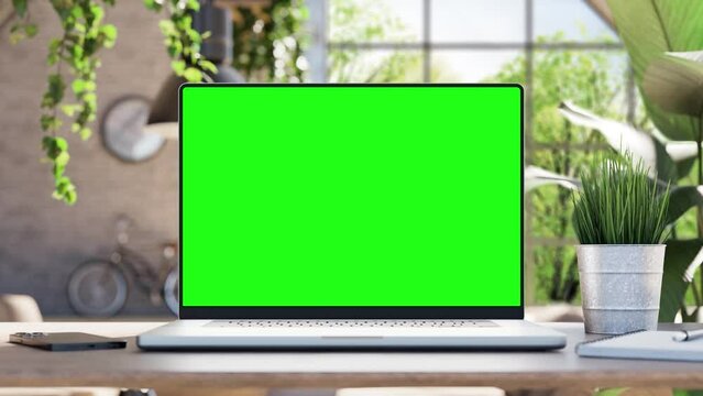 Laptop with blank green screen. Static footage with trees swaying or moving in the wind. Home interior or loft office background, 4k 30fps, looped video
