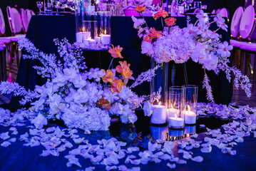 Composition flowers, candles, candlesticks on floor hall restaurant. Table setting, setup. Trendy decor. Birthday, baptism, event. Golden rich interior with light in night. Luxury wedding reception.