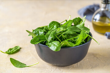 Fresh spinaches in black bowl with olive oil and grey napkin backside on light sand background