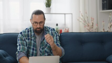 Middle-aged freelancer working on laptop on sofa at home, earning extra income