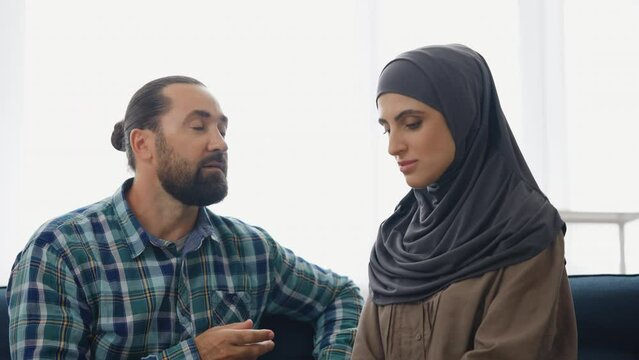 Muslim couple talking at home, obedient wife in hijab nodding head, relationship