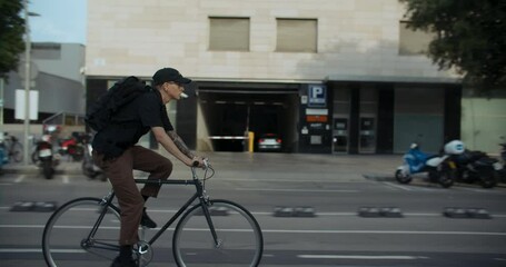Sunny morning side shot of young man in casual clothes ride his bike through city streets on safe bike lane. Urban transportation commuting concept on a bicycle. Green commuter routine