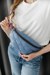 Leather sling bag, Fanny pack woman. Girl in white t-shirt wearing blue banana bag with colored strap, closeup.