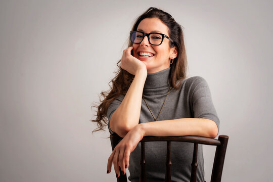 Studio Portrait Of Attractive Brunette Haired Woman Sitting On A Chair At Isolated Background