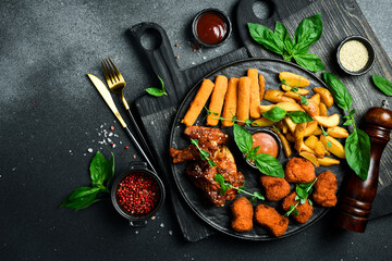 Beer snack plate: chicken nuggets, chicken wings, cheese and fries. On a dark background, close-up.