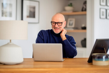 Mid aged man wearing casual clothes and using laptop for work while sitting at home