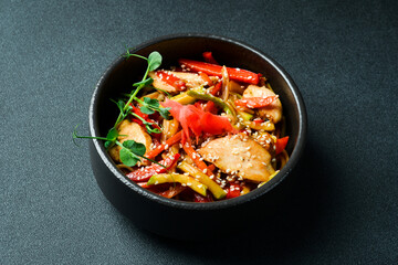 Udon pasta with chicken and ginger. In a black plate. Japanese cuisine. On a dark background, close-up.