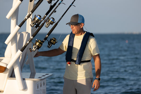 Man on a boat with fishing tackle wearing life jacket.