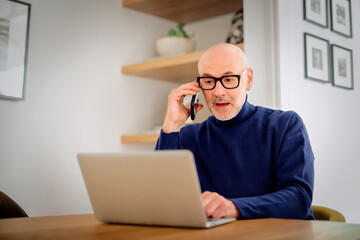Surprised businessman using smartphone and laptop while working from home