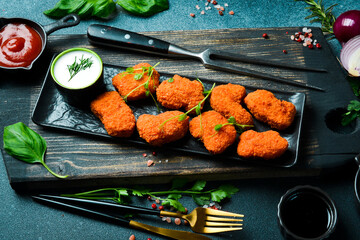 Chicken nuggets with ketchup sauce on a black stone plate. On a dark background, close-up.