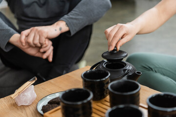 cropped view of woman brewing tea in traditional teapot near tattooed middle aged man.