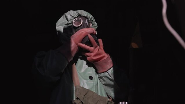 Man puts on black gas mask for special protection from radiation. Specialist gets ready for difficult task to detect radiation in building