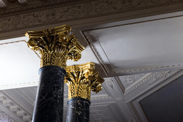 Stone pillars with gold colored capitals are under white ceiling