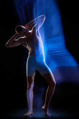 Obraz premium Portrait of young guy wearing underwear and posing in motion over dark background. Mixed neon light