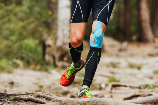 Legs Male Runner With Kinesio Tape On Knee Running Forest Trail Marathon, Black Compression Socks And Blue Kinesiotaping