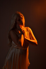 portrait of beautiful blonde woman wearing a fantasy goddess toga costume with  crystal crown.
Backlit a glowing isolated studio background with  orange silhouette lighting.
