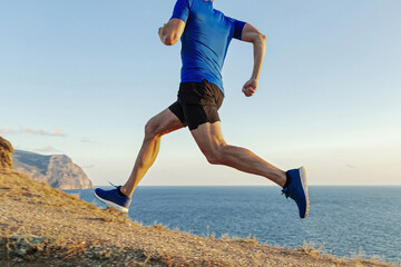 male runner run uphill, sea trail on withered grass, cross-country running race, blue shirt and black shorts