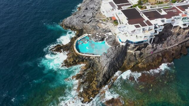 Aerial drone footage of the beautiful town of Costa Adeje, Santa Cruz de Tenerife in Spain showing and old abandoned swimming pool by the ocean and Playa de Ajabo beach in the summer time.