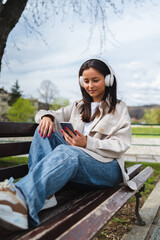 One young girl is listening to music on her wireless headphones and using her phone outdoors