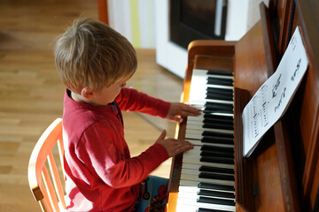 Adorable cute caucasian little toddler boy having playing piano at home. Education, child...