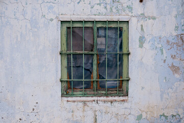 The window of a poor man's house with a grille on a peeled wall painted white with lime