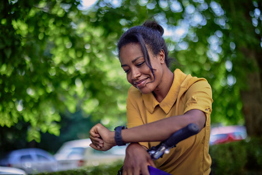 Young woman with a bicycle checking the time on her wristwatch. 