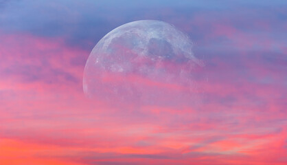 Full moon rising between pink clouds at sunset.