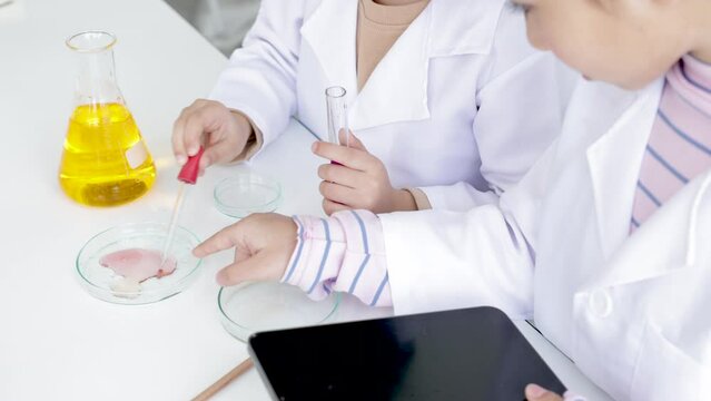 Hand of Elementary schoolgirls with gown uniform scientist imagination having fun with experiment, sibling kids workshop study in laboratory lab, modern lifestyle kids science education concept