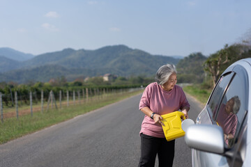 The car ran out of gas and stalled beside the road in suburbs and an elderly Asian woman used a gallon of spare gas to fuel the car. A woman prepares a gallon of spare gas to fuel before traveling.