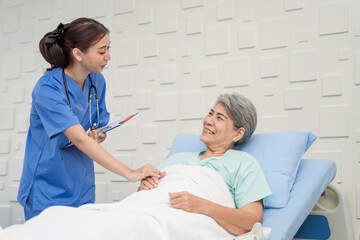 A female nurse or doctor is caring for an elderly female patient lying on the patient's bed doing...