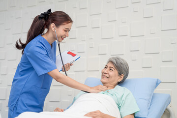 A female nurse or doctor is caring for an elderly female patient lying on the patient's bed doing heart and breathing tests. and the patient has a smile