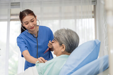 A female nurse or doctor is caring for an elderly female patient lying on the patient's bed doing heart and breathing tests. and the patient has a smile