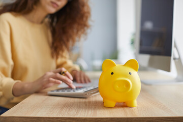 Closeup shot of a cute yellow ceramic piggy bank on a wooden table, with an unrecognizable business...