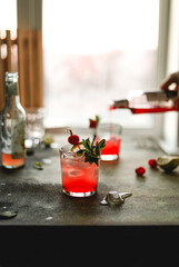 Cooking colorful refreshing fruit and berry cocktails with raspberries, lime, mint and ice on the table with drinks.
