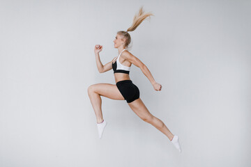 Beautiful fitness woman in a jump in sportswear on a gray background, dynamic movement.