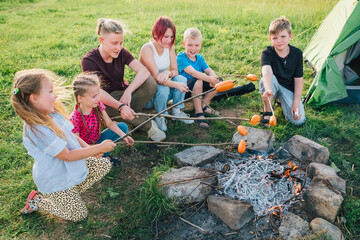 Six kids group Boys and girls cheerfully laughed and roasted sausages on sticks over a campfire...