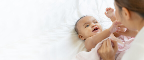 young Asian mother is playing with her newborn baby on the white bed in a home in a morning.Concept...