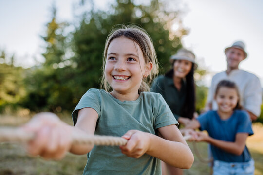 Young family with happy kids having fun together outdoors pulling rope in summer nature.