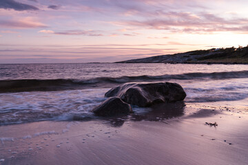 Naklejka premium Sea coast, waves crashing against a stone in the water, sunset