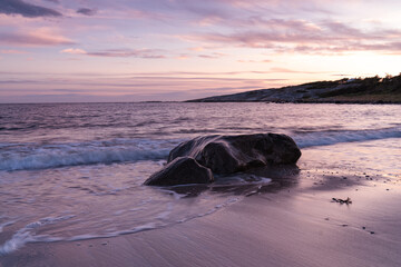 Sea coast, waves crashing against a stone in the water, sunset