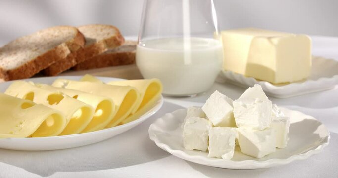 dairy products on a light background. milk cheese bread and butter on a white tablecloth close-up. slices of gouda cheese. piece of butter and a glass of milk with slices of bread in the background.