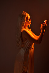 portrait of beautiful blonde woman wearing a fantasy goddess toga costume with  crystal crown.
Backlit a glowing isolated studio background with  orange silhouette lighting.