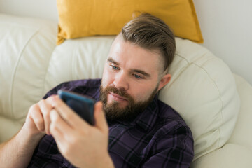 Fototapeta premium Bored lazy man relaxed and use smartphone for killing time alone in apartment - social media and gadget addiction concept