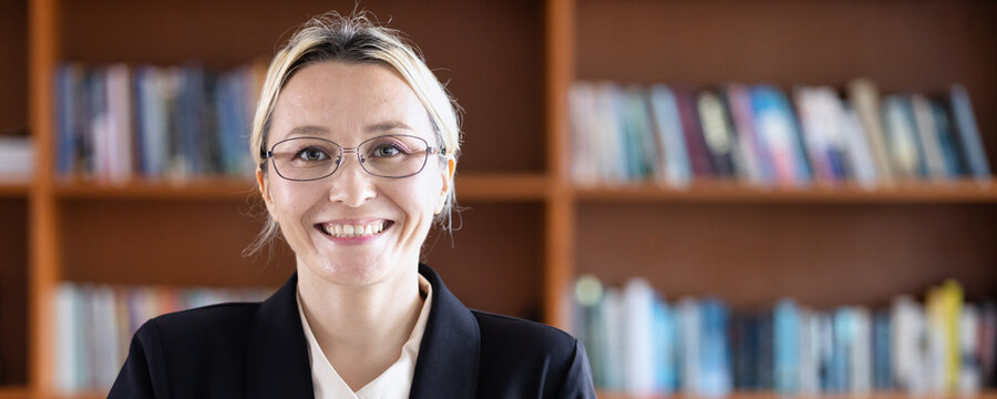 Happy smiling female university professor or librarian with eyeglasses in university library