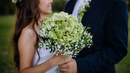 Close-up of bride and groom holding wedding bouquet, outdoor in the meadow.