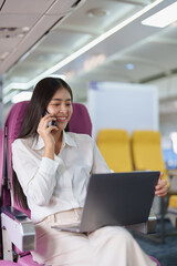 Asian business woman passenger sitting on business class luxury plane while working using smart phone mobile talking or video conference and travel concept