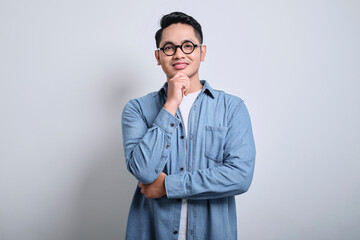 Adult Asian man wearing denim shirt looking at camera with hand on chin showing happy face