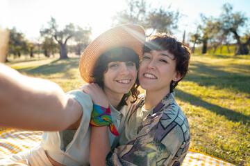 Selfie couple lesbian lgbt smiling enjoying together in nature outdoor with sunset light having picnic