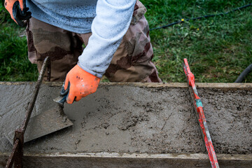 Bricklayer spreading concrete with a trowel and level to build a wall at a construction site